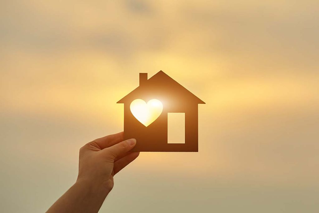 Woman holding a wooden house in front of the sun